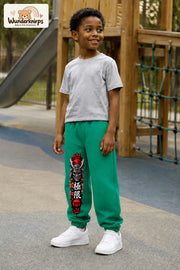 Junge trägt grüne Jogginghose mit Samurai Kirschblüten-Print, leicht seitlich auf dem Spielplatz.