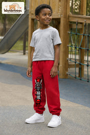 Junge trägt rote Jogginghose mit Samurai Kirschblüten-Print, leicht seitlich auf dem Spielplatz.