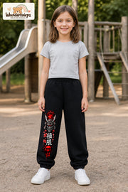 Mädchen trägt schwarze Jogginghose mit Samurai Kirschblüten-Print, von vorn auf dem Spielplatz.