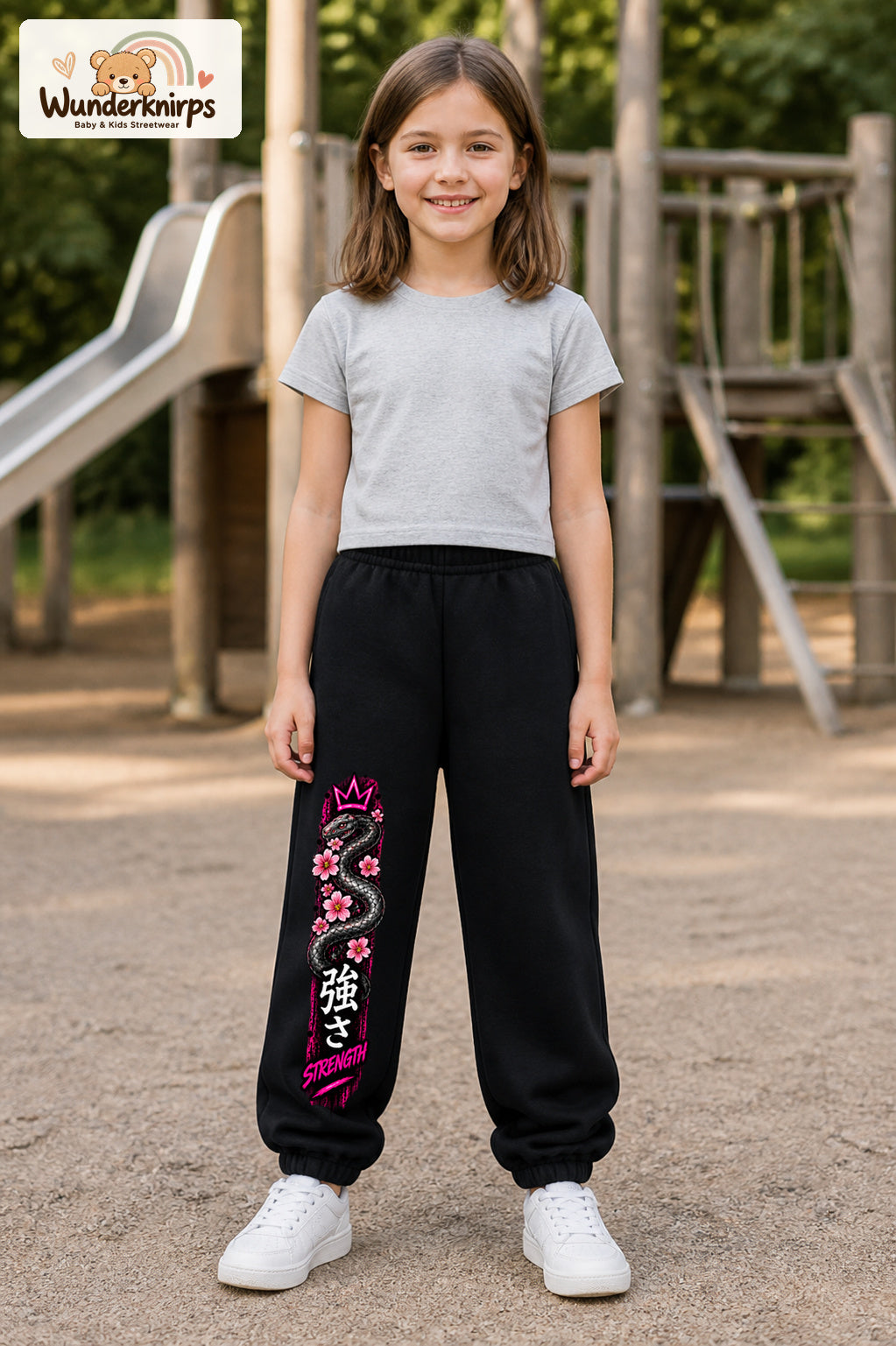 Mädchen trägt schwarze Jogginghose mit Strength Blütenschlange-Print, von vorn auf dem Spielplatz.