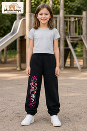 Mädchen trägt schwarze Jogginghose mit Strength Blütenschlange-Print, von vorn auf dem Spielplatz.