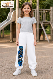 Mädchen trägt weiße Jogginghose mit Beauty in Chaos Rosen-Print, von vorn auf dem Spielplatz.