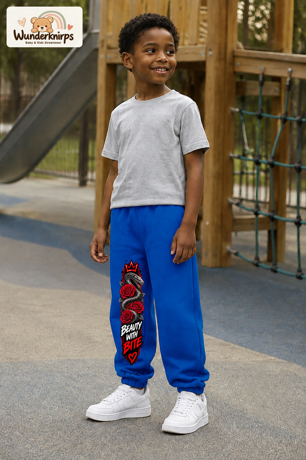 Junge trägt blaue Jogginghose mit Beauty with Bite-Print, leicht seitlich auf dem Spielplatz.