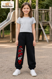 Mädchen trägt schwarze Jogginghose mit Beauty with Bite-Print, von vorn auf dem Spielplatz.