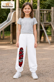 Mädchen trägt weiße Jogginghose mit Beauty with Bite-Print, von vorn auf dem Spielplatz.