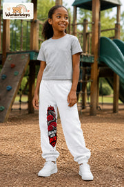 Mädchen trägt weiße Jogginghose mit Beauty with Bite-Print, leicht seitlich auf dem Spielplatz.