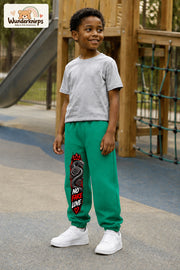 Junge trägt grüne Jogginghose mit No Fake Love Schlange-Print, leicht seitlich auf dem Spielplatz.