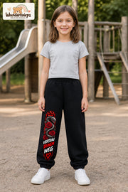 Mädchen trägt schwarze Jogginghose mit Vertrau deinem Weg-Print, von vorn auf dem Spielplatz.