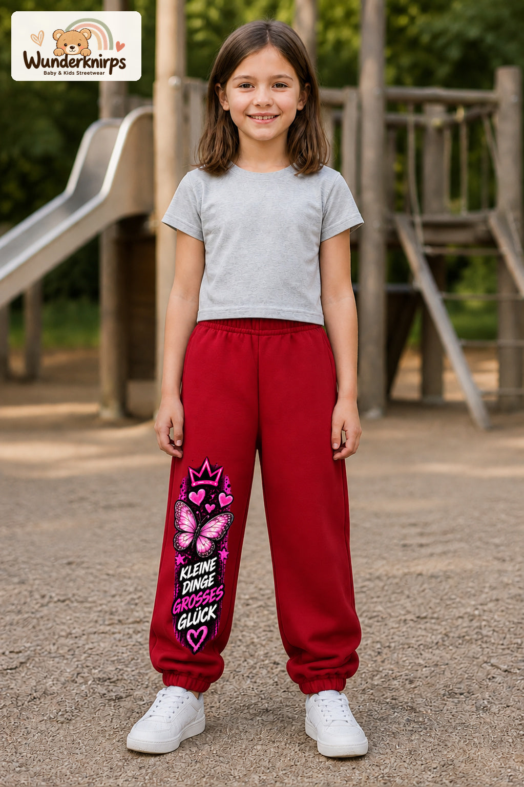 Mädchen trägt rote Jogginghose mit Kleine Dinge Schmetterling-Print, von vorn auf dem Spielplatz.