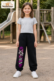 Mädchen trägt schwarze Jogginghose mit Großes Glück Lilie-Print, von vorn auf dem Spielplatz.