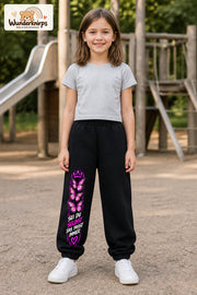 Mädchen trägt schwarze Jogginghose mit Sei du selbst Falter-Print, von vorn auf dem Spielplatz.