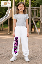 Mädchen trägt weiße Jogginghose mit Sei du selbst Falter-Print, von vorn auf dem Spielplatz.