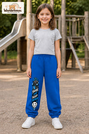 Mädchen trägt blaue Jogginghose mit Skate Eat Sleep Repeat-Print, von vorn auf dem Spielplatz.