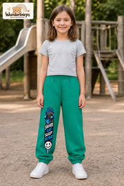 Mädchen trägt grüne Jogginghose mit Skate Eat Sleep Repeat-Print, von vorn auf dem Spielplatz.