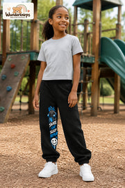 Mädchen trägt schwarze Jogginghose mit Skate Eat Sleep Repeat-Print, leicht seitlich auf dem Spielplatz.