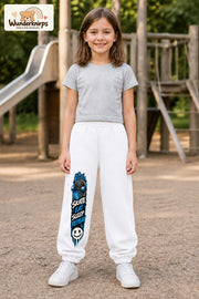 Mädchen trägt weiße Jogginghose mit Skate Eat Sleep Repeat-Print, von vorn auf dem Spielplatz.