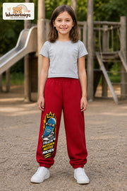 Mädchen trägt rote Jogginghose mit Aufstehen Skateboard-Print, von vorn auf dem Spielplatz.