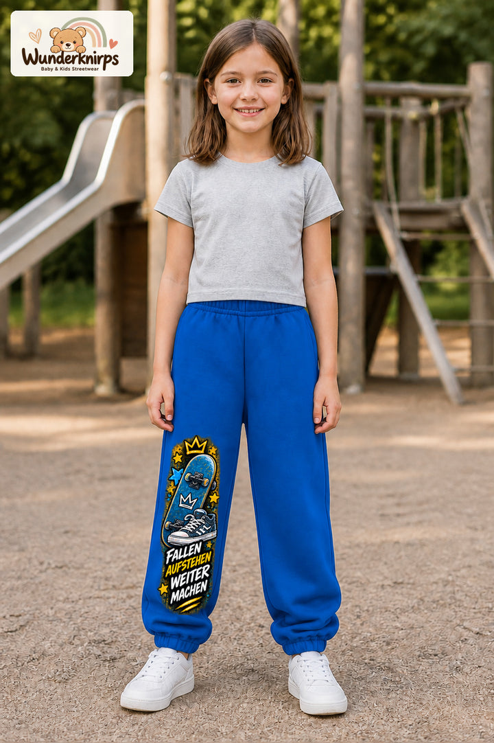 Mädchen trägt blaue Jogginghose mit Weitermachen Sternen-Board-Print, von vorn auf dem Spielplatz.