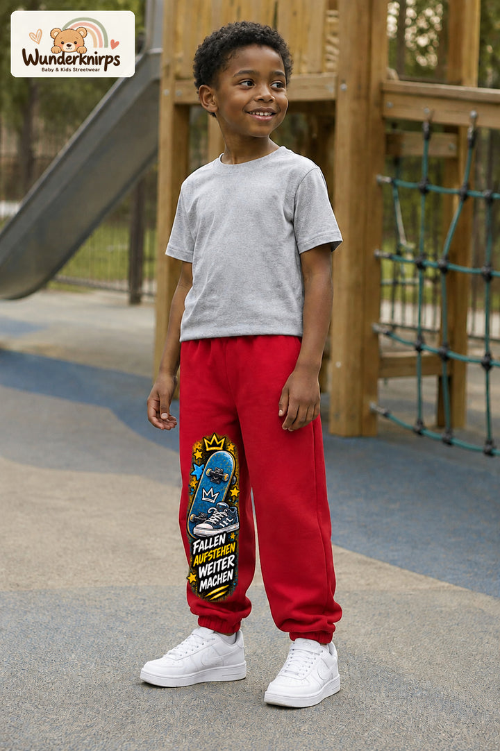 Junge trägt rote Jogginghose mit Weitermachen Sternen-Board-Print, leicht seitlich auf dem Spielplatz.