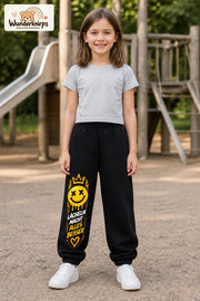 Mädchen trägt schwarze Jogginghose mit Lächeln macht besser-Print, von vorn auf dem Spielplatz.