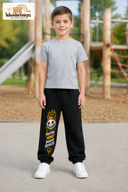 Junge trägt schwarze Jogginghose mit Positive Mind Smiley-Print, von vorn auf dem Spielplatz.