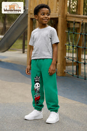 Junge trägt grüne Jogginghose mit Never Stop Smiley-Print, leicht seitlich auf dem Spielplatz.