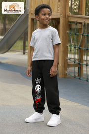 Junge trägt schwarze Jogginghose mit Never Stop Smiley-Print, leicht seitlich auf dem Spielplatz.