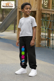 Junge trägt schwarze Jogginghose mit Good Kids Smileys-Print, leicht seitlich auf dem Spielplatz.