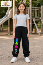 Mädchen trägt schwarze Jogginghose mit Good Kids Smileys-Print, von vorn auf dem Spielplatz.