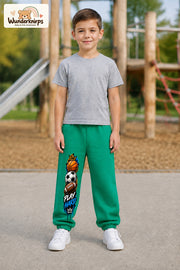 Junge trägt grüne Jogginghose mit Play Hard Sportmix-Print, von vorn auf dem Spielplatz.