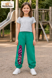 Mädchen trägt grüne Jogginghose mit Girl Boss Bär-Print, von vorn auf dem Spielplatz.