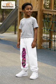 Junge trägt weiße Jogginghose mit Girl Boss Bär-Print, leicht seitlich auf dem Spielplatz.