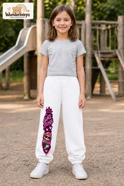 Mädchen trägt weiße Jogginghose mit Girl Boss Bär-Print, von vorn auf dem Spielplatz.