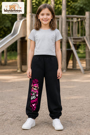 Mädchen trägt schwarze Jogginghose mit Girl Power Teddy-Print, von vorn auf dem Spielplatz.