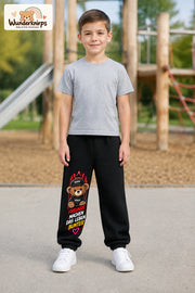 Junge trägt schwarze Jogginghose mit Freunde machen bunt Teddy-Print, von vorn auf dem Spielplatz.