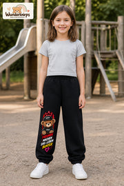 Mädchen trägt schwarze Jogginghose mit Freunde machen bunt Teddy-Print, von vorn auf dem Spielplatz.