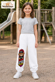 Mädchen trägt weiße Jogginghose mit Freunde machen bunt Teddy-Print, von vorn auf dem Spielplatz.