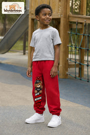Junge trägt rote Jogginghose mit Gute Freunde Teddy-Print, leicht seitlich auf dem Spielplatz.