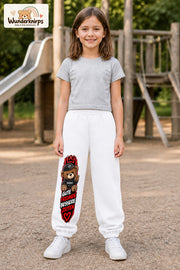 Mädchen trägt weiße Jogginghose mit Gute Freunde Teddy-Print, von vorn auf dem Spielplatz.