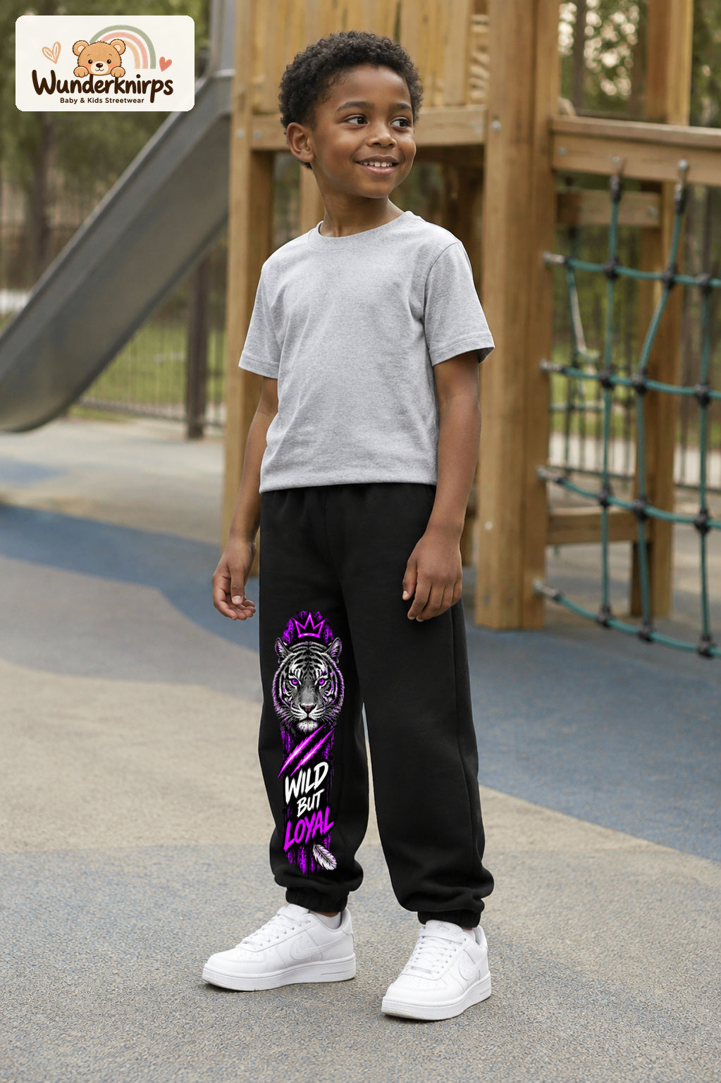 Junge trägt schwarze Jogginghose mit Wild but Loyal Tiger-Print, leicht seitlich auf dem Spielplatz.