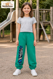 Mädchen trägt grüne Jogginghose mit Stay Wild Schmetterlingstiger-Print, von vorn auf dem Spielplatz.