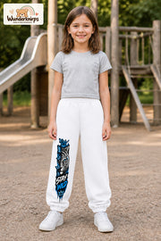 Mädchen trägt weiße Jogginghose mit Stay Wild Schmetterlingstiger-Print, von vorn auf dem Spielplatz.