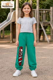 Mädchen trägt grüne Jogginghose mit Bad Vibes Skull-Print, von vorn auf dem Spielplatz.