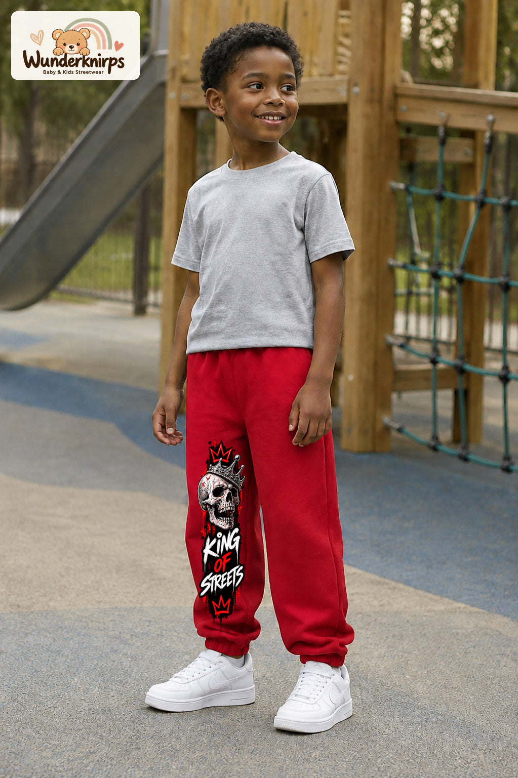 Junge trägt rote Jogginghose mit King of Streets Skull-Print, leicht seitlich auf dem Spielplatz.