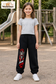 Mädchen trägt schwarze Jogginghose mit Fearless Totenkopf-Print, von vorn auf dem Spielplatz.