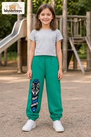 Mädchen trägt grüne Jogginghose mit Trust Your Instincts Wolf-Print, von vorn auf dem Spielplatz.