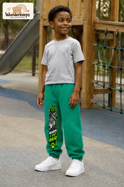 Junge trägt grüne Jogginghose mit Always Ahead Wolf-Print, leicht seitlich auf dem Spielplatz.