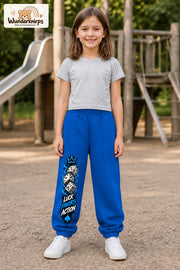 Mädchen trägt blaue Jogginghose mit Luck Favors Würfel-Print, von vorn auf dem Spielplatz.