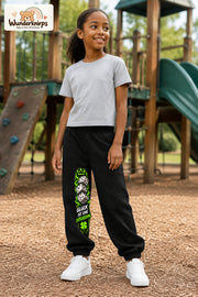 Mädchen trägt schwarze Jogginghose mit Glück ist Entscheidung-Print, leicht seitlich auf dem Spielplatz.