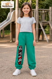 Mädchen trägt grüne Jogginghose mit Risk More Würfel-Print, von vorn auf dem Spielplatz.